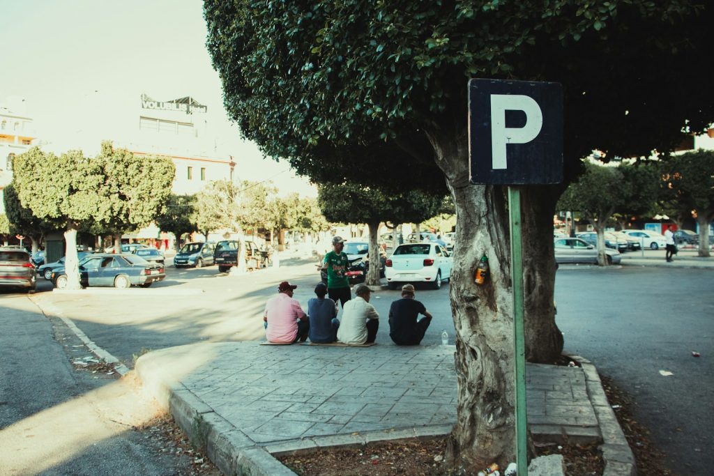 A group of people sitting on a sidewalk next to a tree