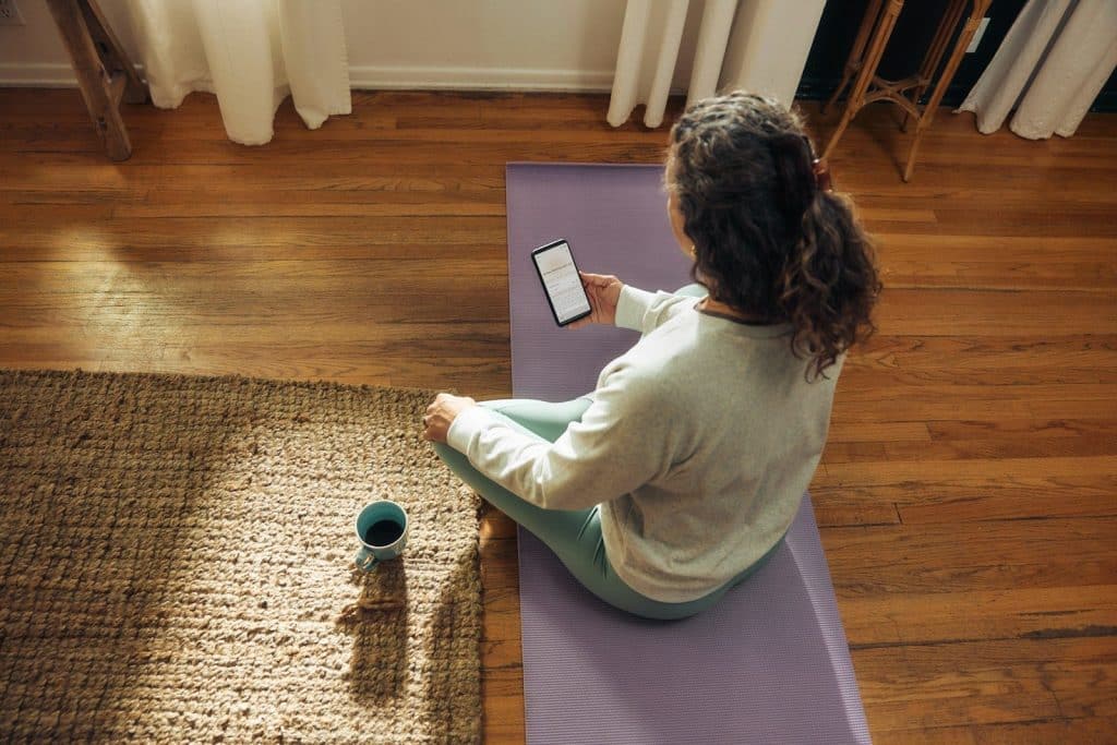 Woman meditating on yoga mat with phone and drink