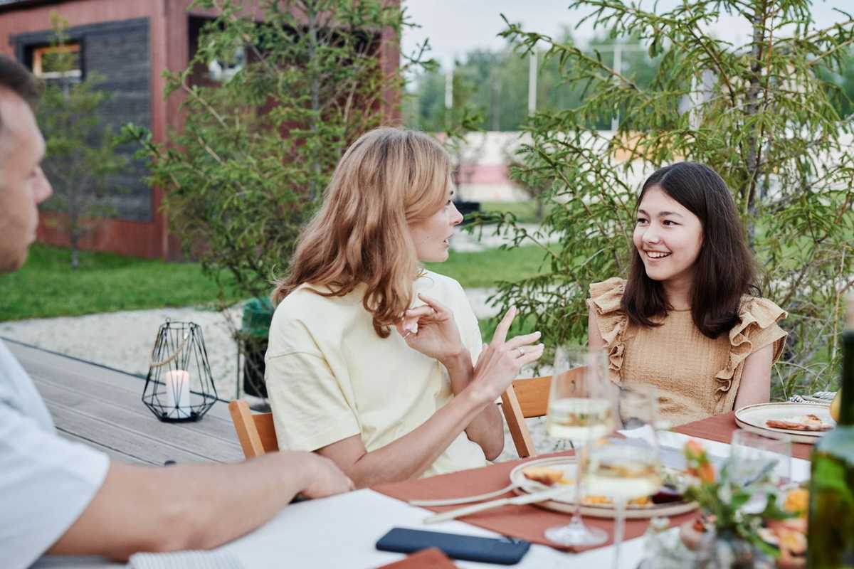 Groupe de personnes mangeant dehors, verres et assiette sur la table, téléphone et végétation environnante Groupe de personnes mangeant dehors, verres et assiette sur la table, téléphone et végétation environnante