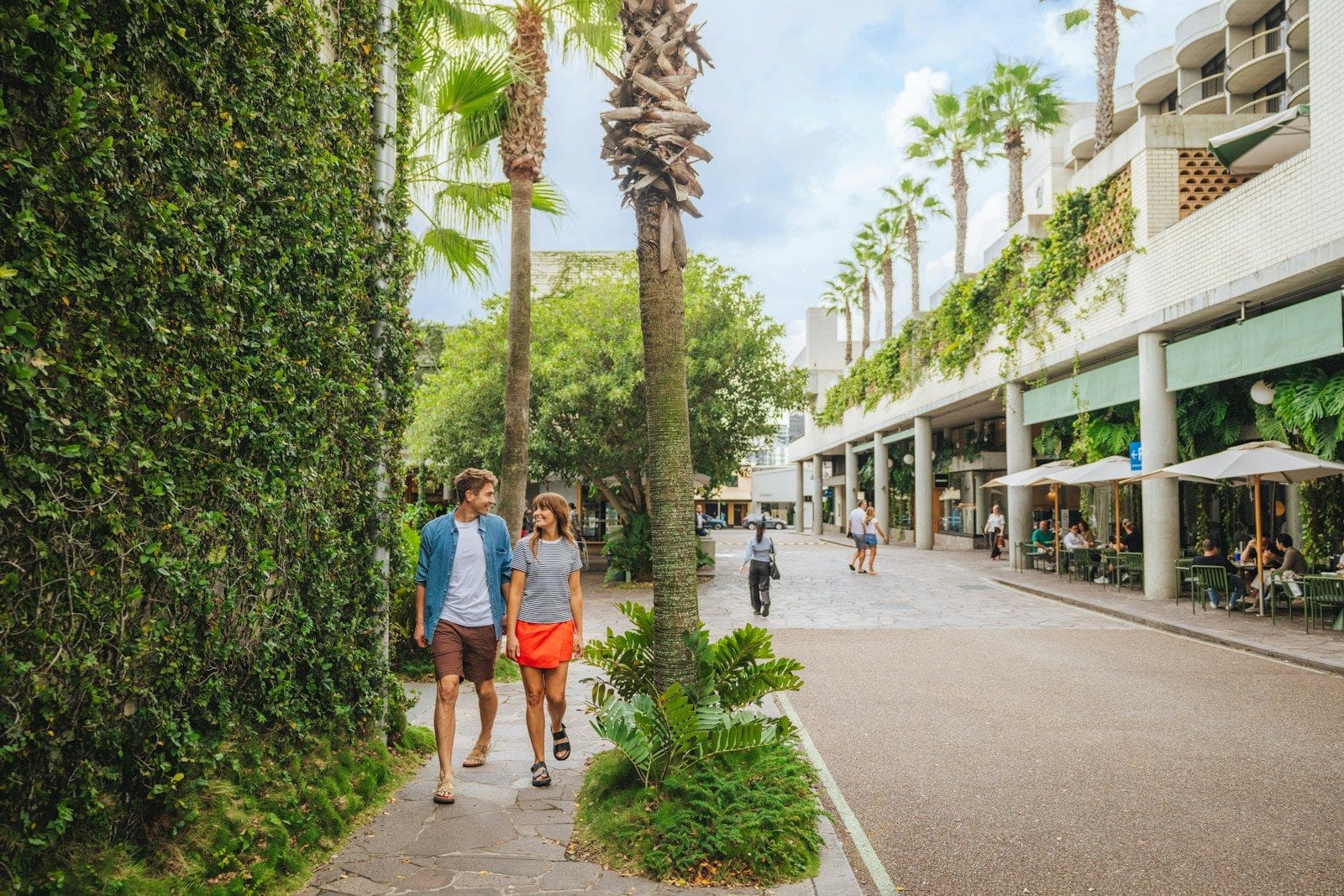 Bien-être professionnel A man and a woman walking along a palm-lined path beside a green wall